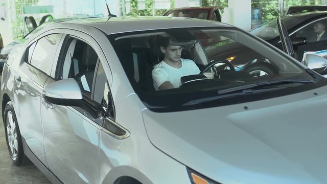 Young guy inspects auto cabin in the car dealership