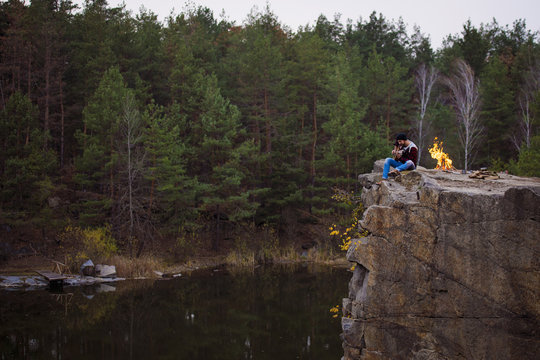 young handsome attractive bearded model man playing guitar in forest with bonfire. Casual man, life style. Beautiful view on forest and rock