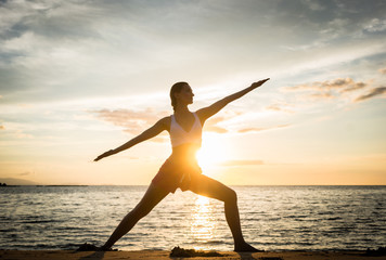 Full length side view of the silhouette of a fit woman practicing the warrior yoga pose against sky...