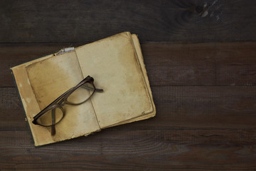 open book and pair of old glasses on a old wooden table top
