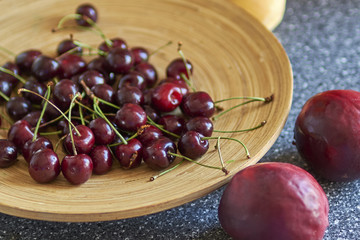 Cherry in a wooden plate and other fruits in the background