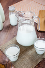 milk and glasses of milk on a wooden rustic table.