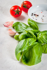 Food background. Ingredients, greens and spices for cooking lunch, lunch. Fresh basil leaves, tomatoes, garlic, onions, salt, pepper. On a white stone table. Copy space