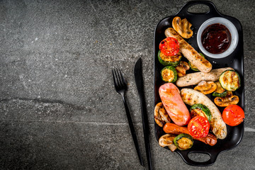 Barbecue. Assortment of various grilled meat sausages, with vegetables BBQ - mushrooms, tomatoes, zucchini, onions. On a black stone table, on a black plate, with sauce. Copy space top view