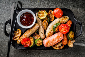 Barbecue. Assortment of various grilled meat sausages, with vegetables BBQ - mushrooms, tomatoes, zucchini, onions. On a black stone table, on a black plate, with sauce. Copy space top view