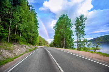 Fototapeta na wymiar highway near the lake and forest. on the horizon rainbow