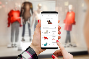 Girl shopping shoes online in front of boutique on her smartphone