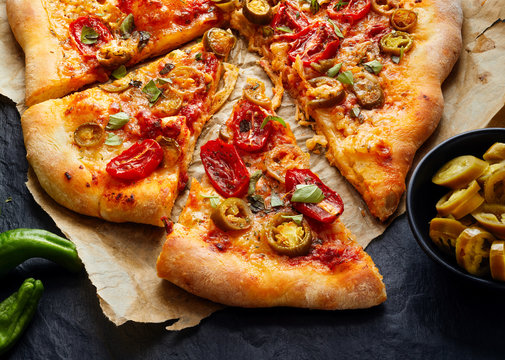 Jalapeno pizza with tomatoes and herbs on a black background, top view
