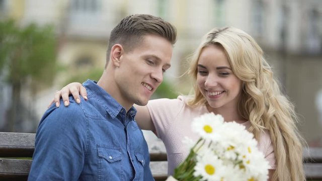 Young man waiting for girlfriend on bench, giving her flowers, happy couple