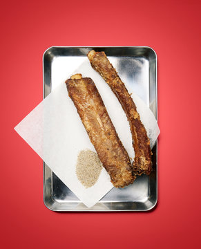 two ribs with spice on metal tray, on red background, studio
