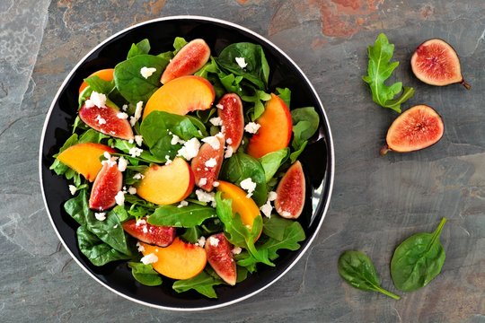 Autumn Salad Of Arugula, Spinach Figs And Goat Cheese In A Black Plate, Above View On A Slate Background