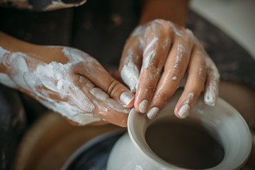 Dirty hands in white clay, pottery wheel with bowl or jar. Potter at work, woman's hands