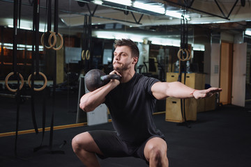 Pretty young man doing squats with dumbbell at the gym