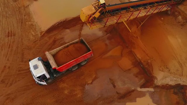 Mining conveyor loading sand in dump truck. Sand work. Mining conveyor belt pouring sand in dump truck at quarry. Mining industry. Aerial view of sand mining process