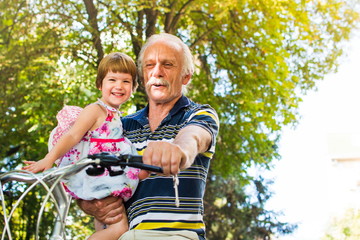 Grandpa riding bicycle with granddaughter in hands