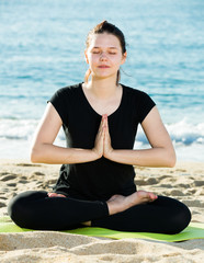 Fototapeta na wymiar Smiling adult woman in black T-shirt is sitting and doing meditation