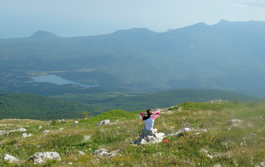 Naklejka premium A young girl sits on edge cliff and looking at mountain landscape
