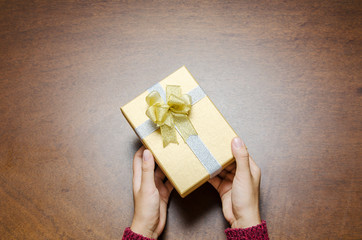 Woman holding golden gift box in hand on wooden background to giving in holidays