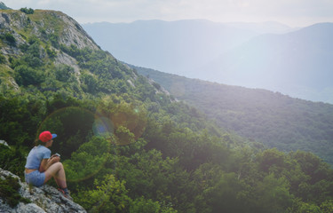Obraz premium A young girl sits on edge cliff and looking at mountain landscape