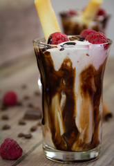 Delicious milkshake with ice cream, raspberries, chocolate, cinnamon and coffee beans on wooden background. Close-up