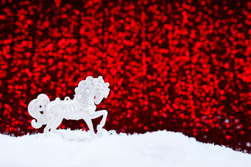 Christmas card on a red background. White toy horse in the snow..
