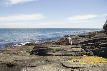 Contemplative man sitting on a rock formation gazing at the Pacific Ocean