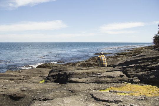 Contemplative man sitting on a rock formation gazing at the Pacific Ocean