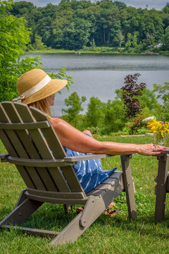 Woman In Sunhat Sitting In Adirondack Chair Looking At Lake