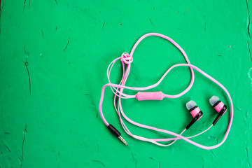 White, pink stereo earphones on wooden green background, copy space for text