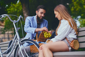A couple eats grape on a bench in a park.