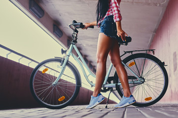 Close up image of tan woman's legs and a bicycle on a pink concrete tunnel road.