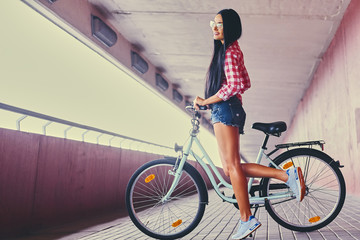 A woman posing on a bicycle in a tunnel with pink walls.