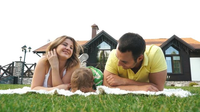 Happy family outdoors on the grass in a park, smiling faces all lying down having fun