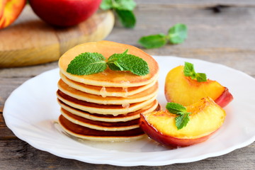 Stack of sweet pancakes with syrup and grilled nectarines slices on a serving plate. Simple pancake recipe. Tasty breakfast or brunch for kids and whole family. Closeup