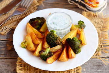 Roasted potatoes and broccoli with dill sour cream on a plate and a wooden table. Simple roasted potatoes and broccoli recipe idea. Rustic style. Closeup