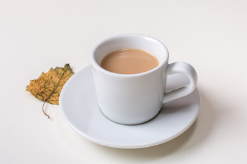 Isolated cup of coffee on saucer with autumn fallen yellow leaf on white background.