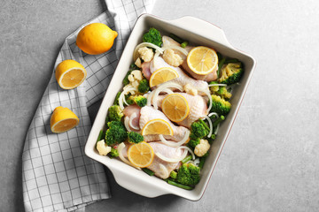 Raw chicken drumsticks with lemon and broccoli in baking dish on grey table
