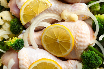 Raw chicken drumsticks with lemon and broccoli, closeup