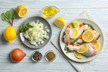 Raw chicken drumsticks with lemon and ingredients on light wooden table
