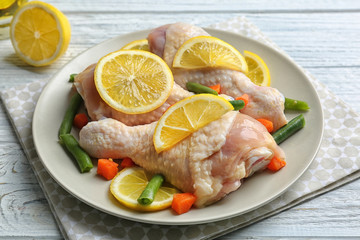 Plate with raw chicken drumsticks and lemon on light wooden table