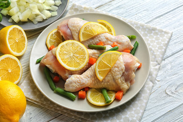 Plate with raw chicken drumsticks and lemon on light wooden table