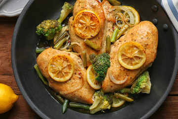 Delicious chicken with lemon and vegetables in frying pan on wooden table
