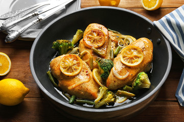 Delicious chicken with lemon and vegetables in frying pan on wooden table
