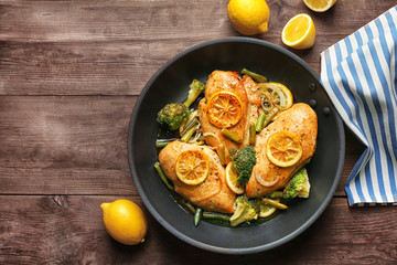 Delicious chicken with lemon and vegetables in frying pan on wooden table