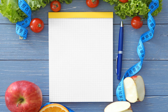 Blank notebook, healthy fresh food and measuring tape on wooden table. Weight loss concept
