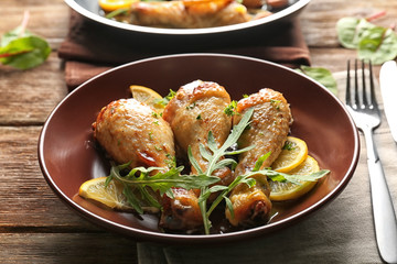 Plate with delicious roasted chicken drumsticks and sliced lemon on wooden table