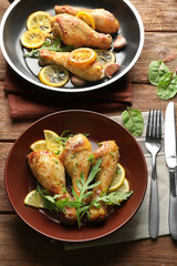 Plate and frying pan with delicious roasted chicken drumsticks on wooden table