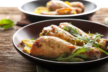 Plate with delicious roasted chicken drumsticks and sliced lemon on wooden table