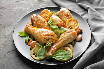 Plate with delicious roasted chicken drumsticks and lemon on grey table