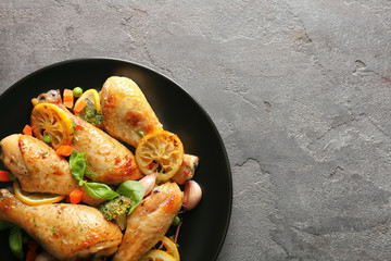 Plate with delicious roasted chicken drumsticks and lemon on grey table